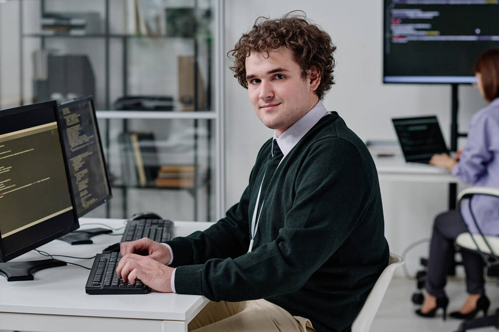 IT specialist looking at the camera while typing code at an office workstation